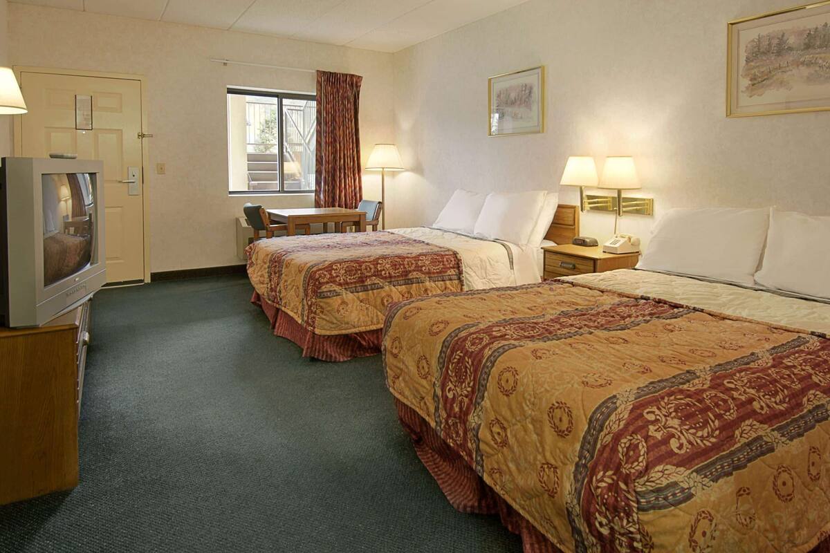 A hotel room with two beds, a desk, a chair, a television, and a window with curtains.