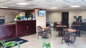 A reception area with a wooden desk, several chairs, a coffee machine, and a television screen displaying a news broadcast. - Days Inn by Wyndham Morehead (Morehead)