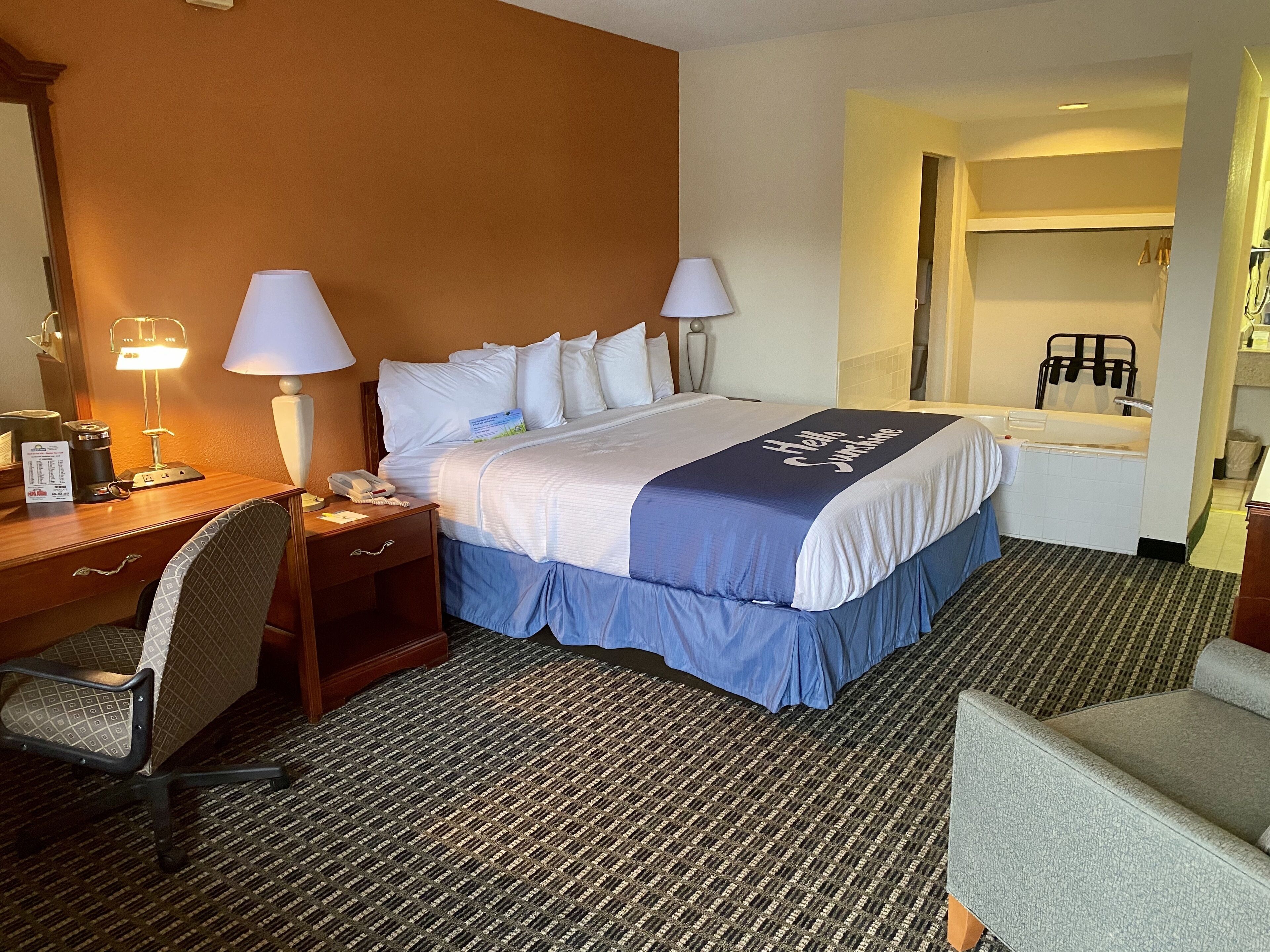 Een hotelkamer met een bed, bureau, stoel en een badkamer zichtbaar door een open deur.