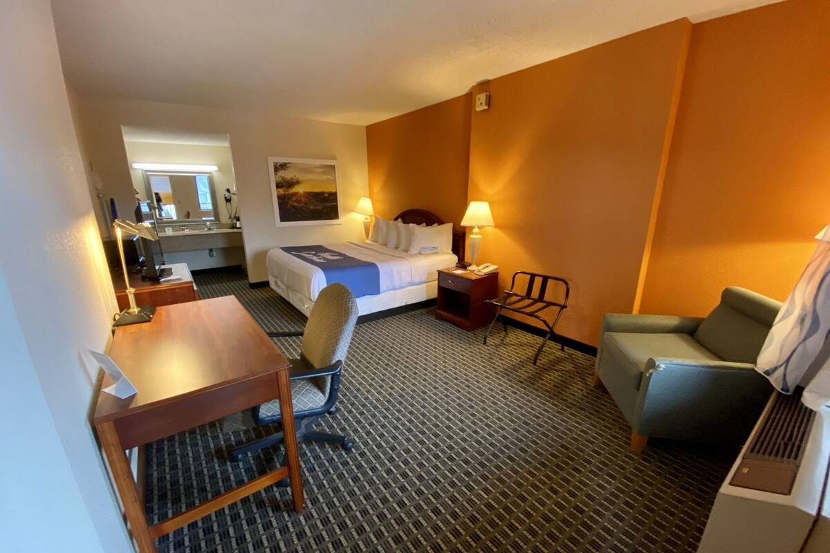 A hotel room with a bed, desk, chair, and a small table.