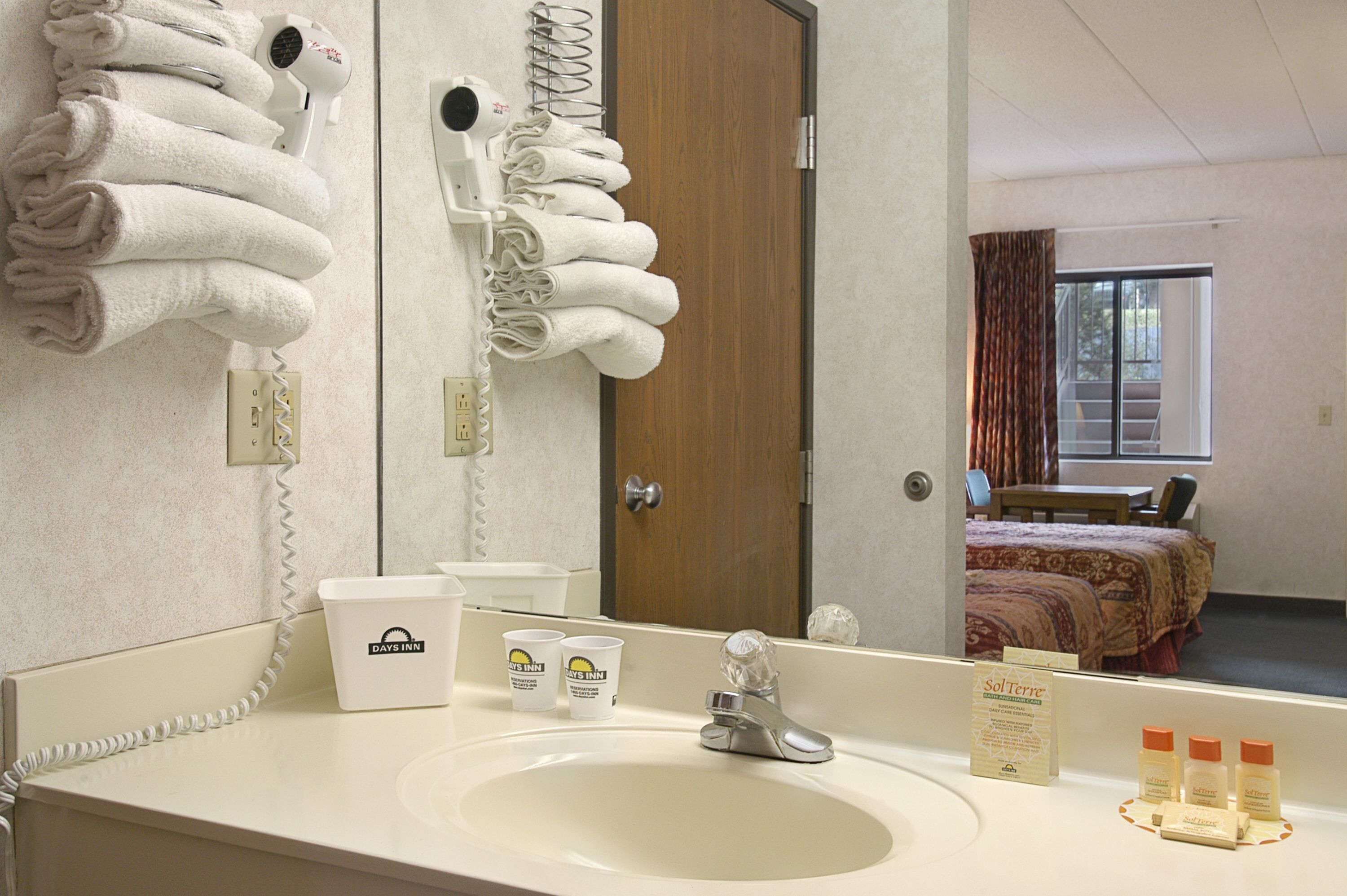 A hotel bathroom with a sink, mirror, towel rack, hair dryer, and toiletries.