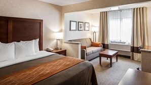 Una habitación de hotel con una cama grande, un sofá, un escritorio y una ventana con cortinas.