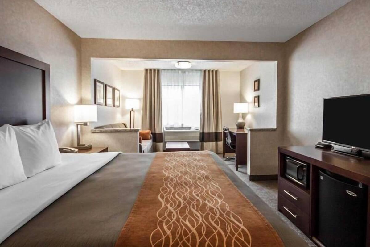 A hotel room with a bed, a desk, a TV, a microwave, and a refrigerator.