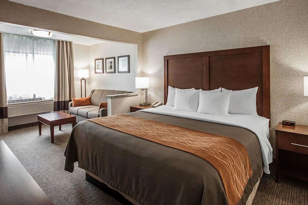 A hotel room with a large bed, a desk, a chair, and a window with curtains.
