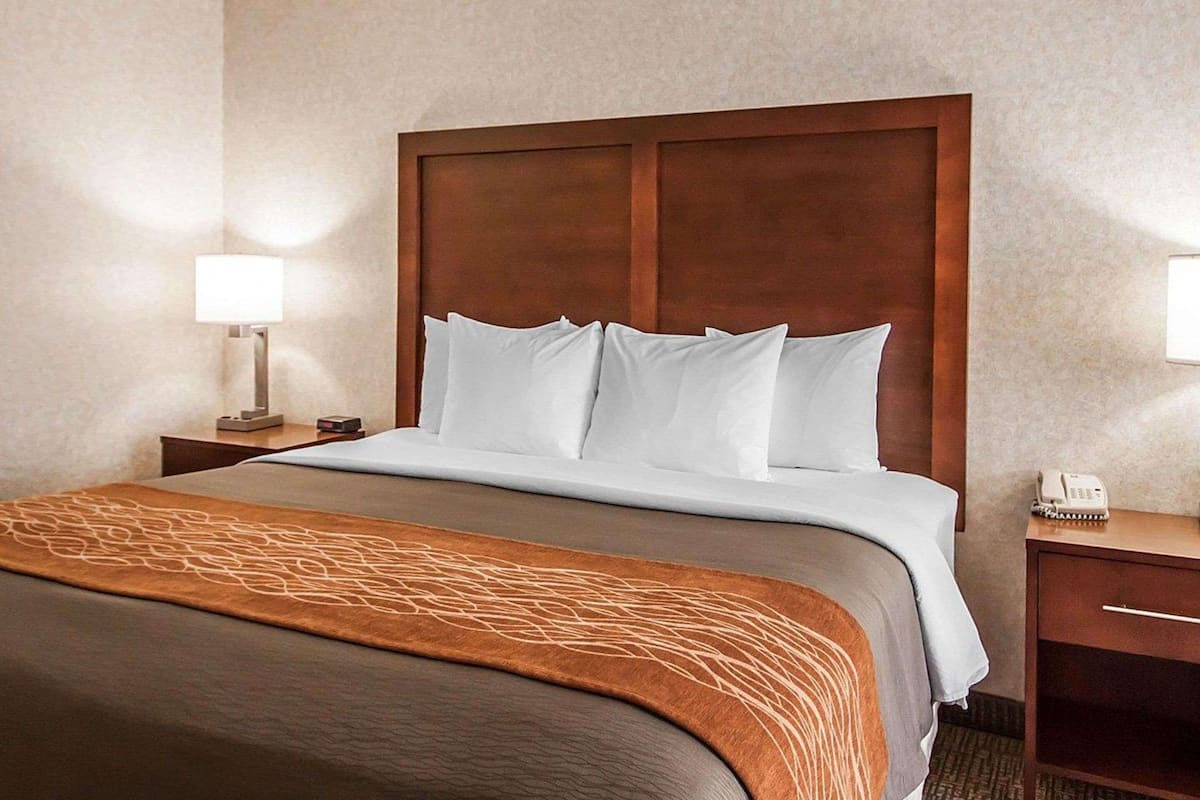 A hotel room with a large bed, wooden headboard, two bedside tables, a lamp, and a telephone.