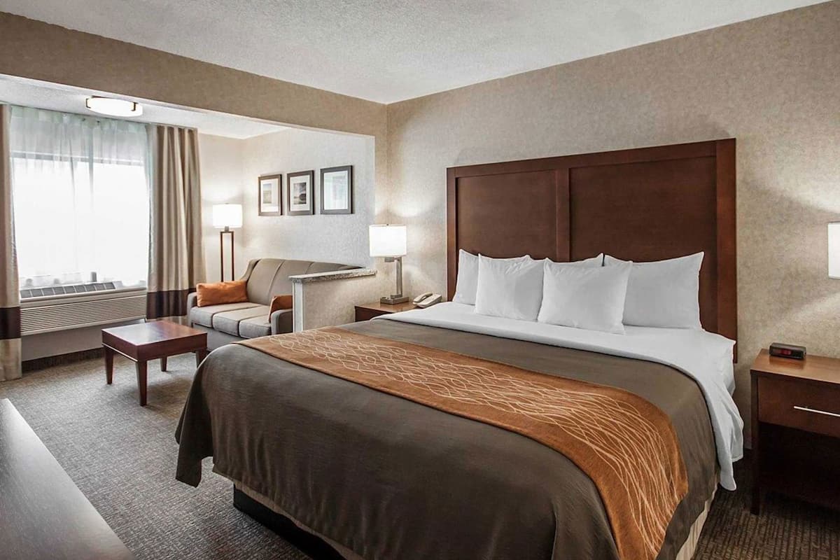 A hotel room with a large bed, a desk, a chair, a desk lamp, and a window with curtains.