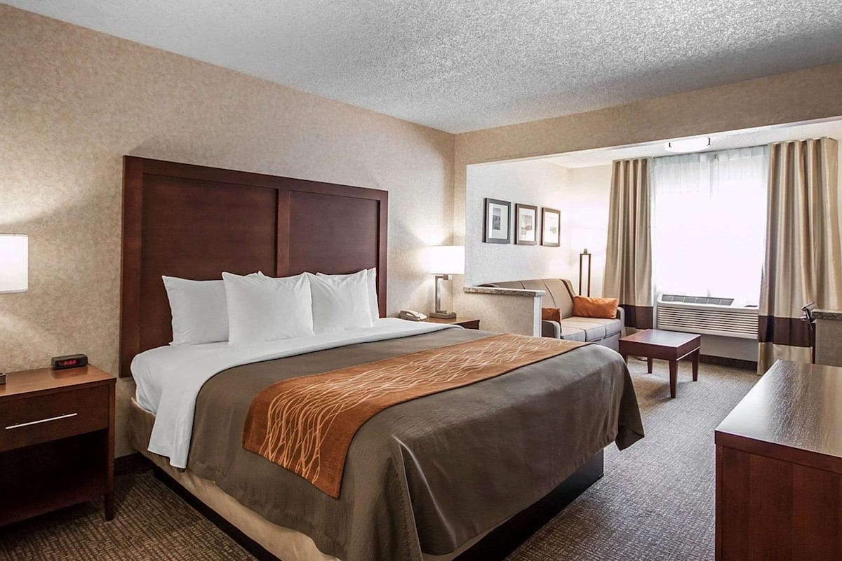 A hotel room with a large bed, bedside tables, a desk, a chair, and a window with curtains.
