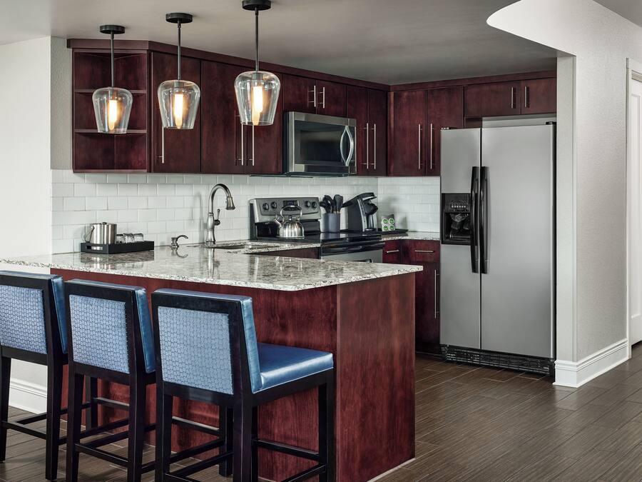 A kitchen with dark wood cabinets, a stainless steel refrigerator, a microwave, and a large island with bar stools.