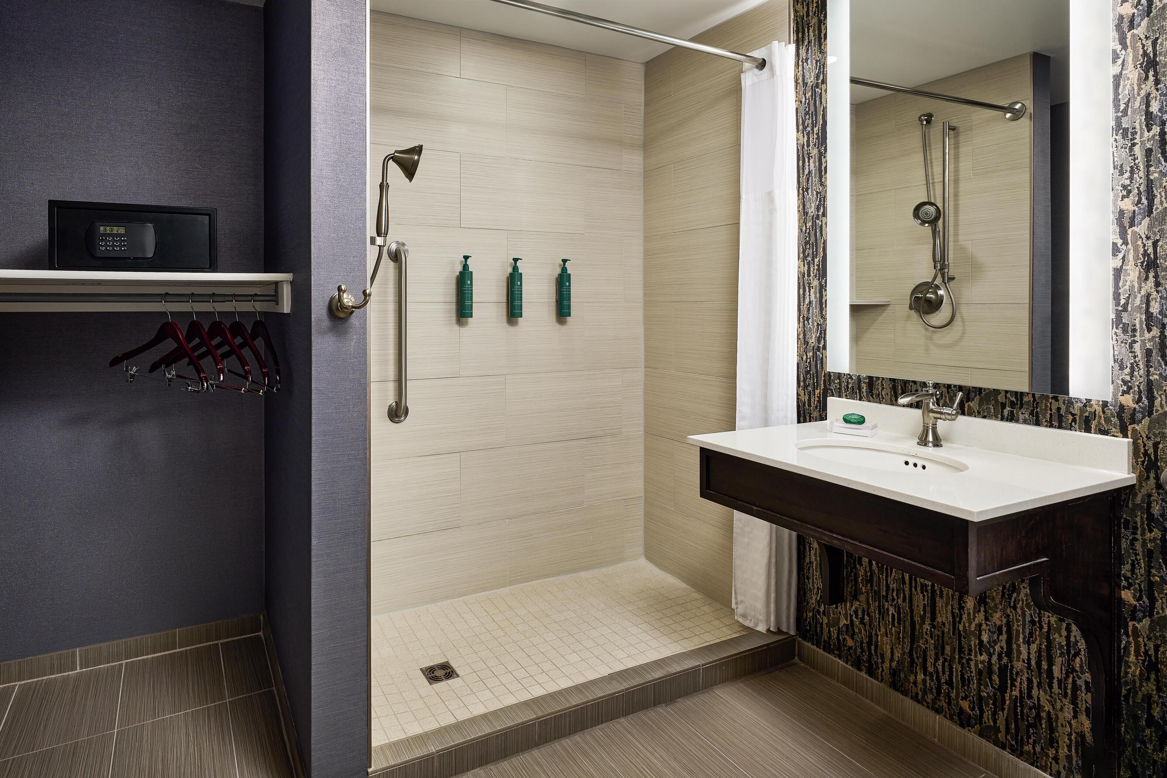 A modern bathroom with a shower, a vanity with a mirror, and a shelf with toiletries.