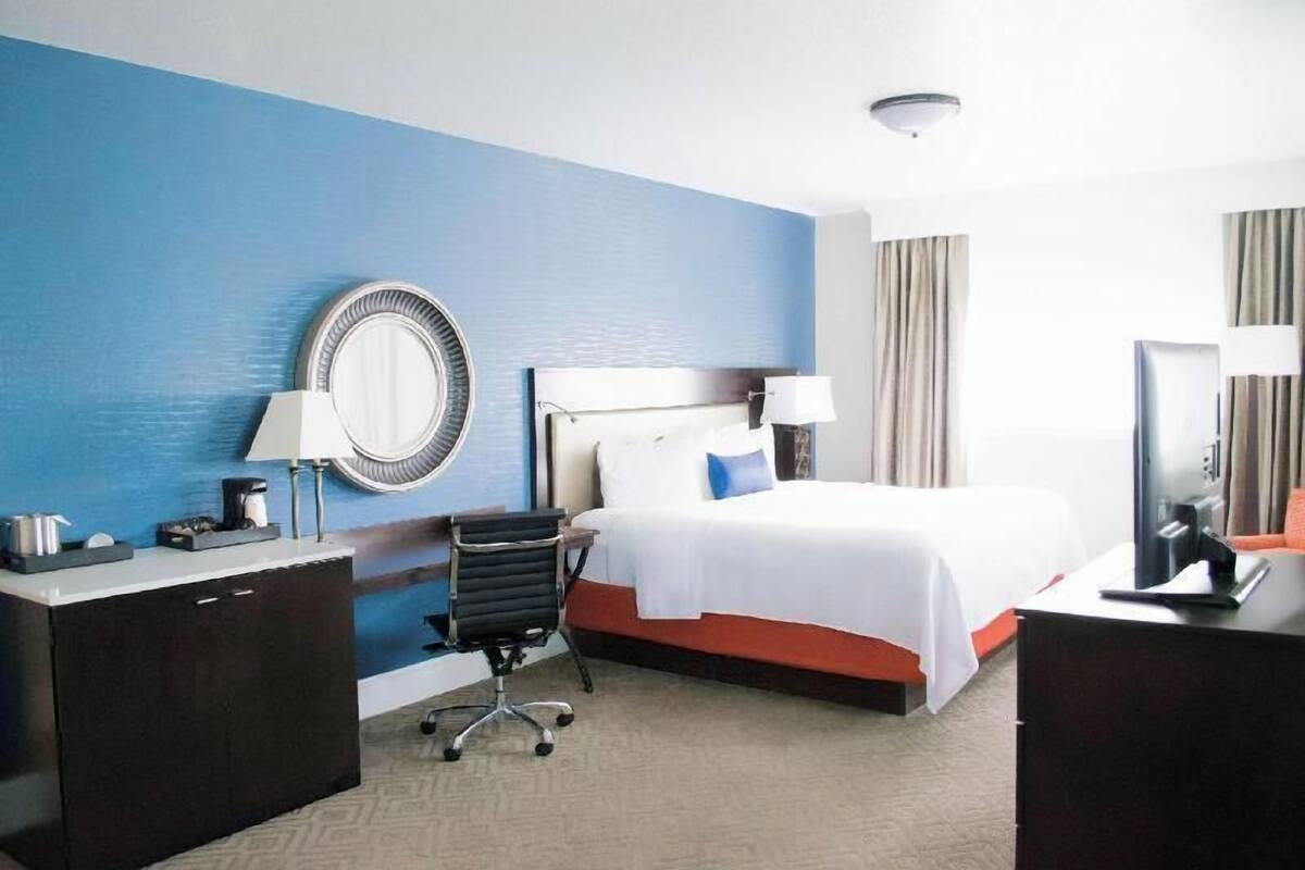 A hotel room with a bed, a desk, a chair, a mirror, and a television.