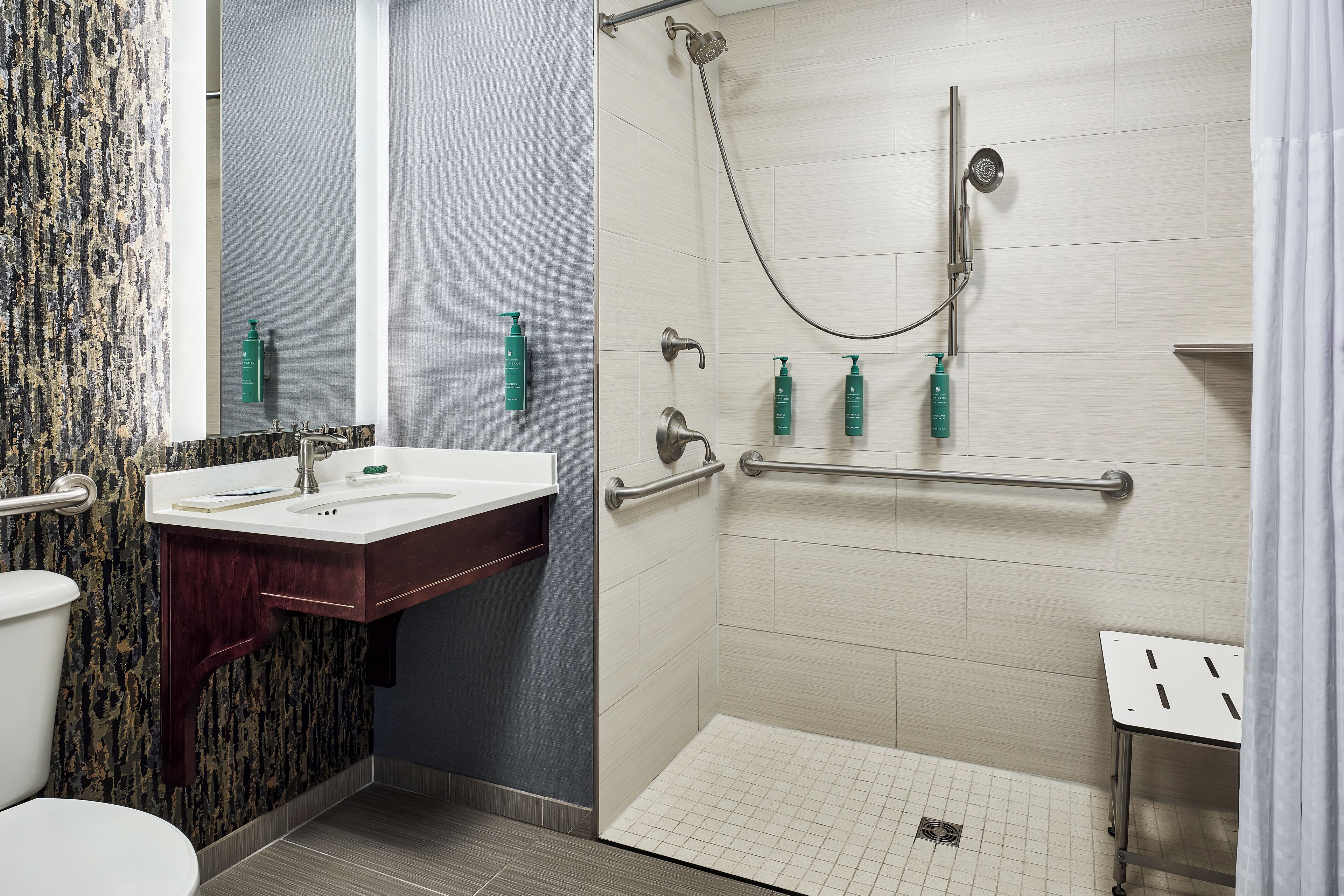 A bathroom with a shower, toilet, sink, and handrails.
