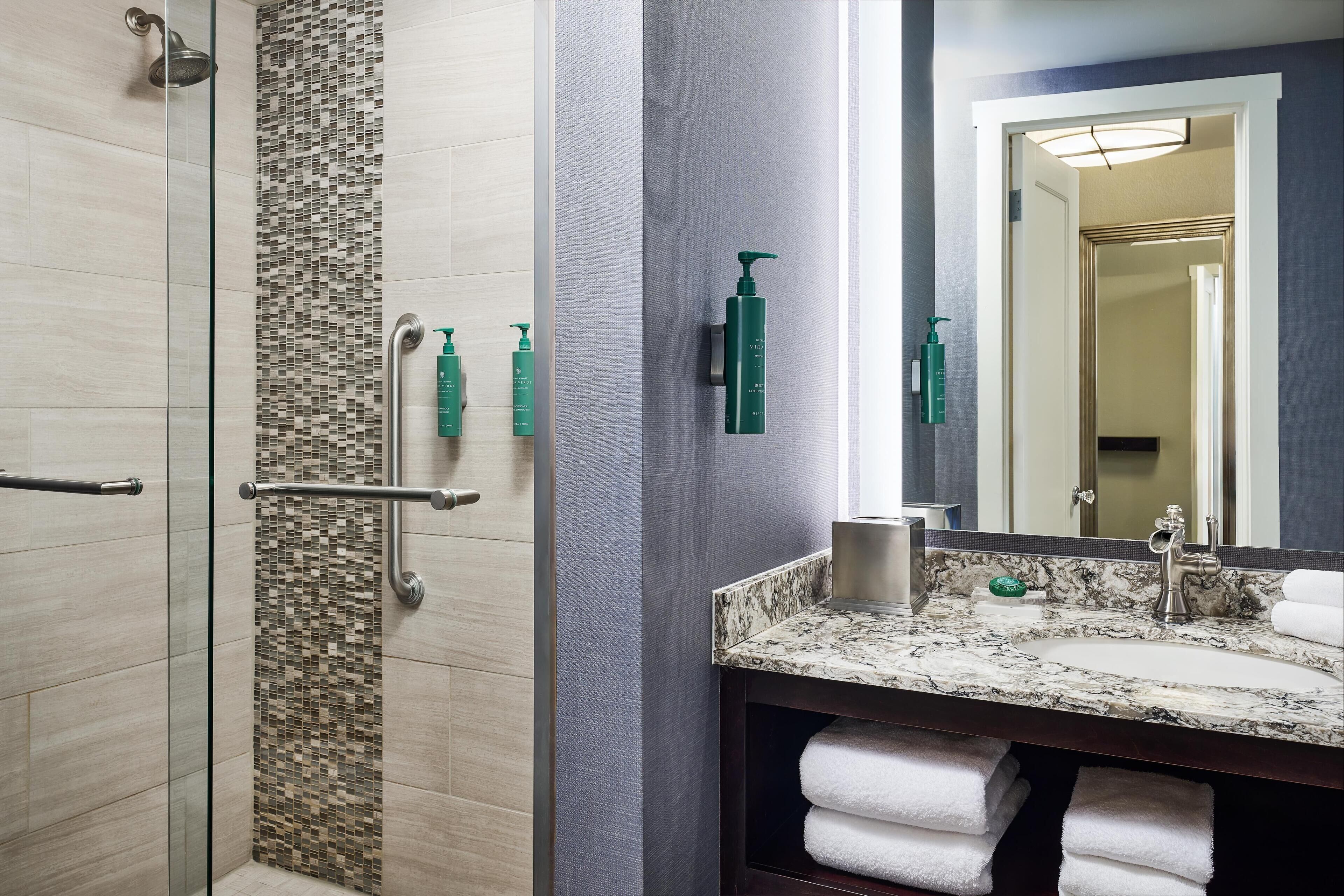 A bathroom with a shower, a sink, a mirror, and toiletries.