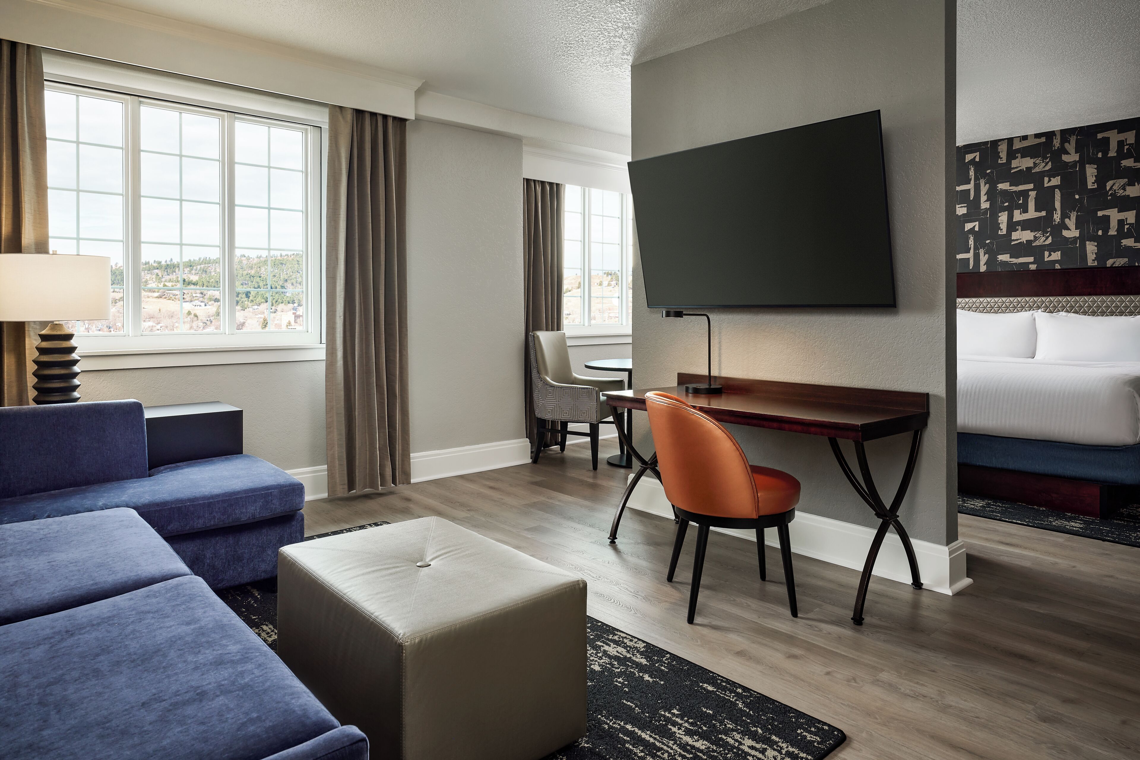 Ein Hotelzimmer mit Sofa, Hocker, Esstisch, Stühlen, Fernseher und Bett.