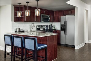 Una cocina con armarios de madera oscura, electrodomésticos de acero inoxidable, una isla de mármol y taburetes de bar.