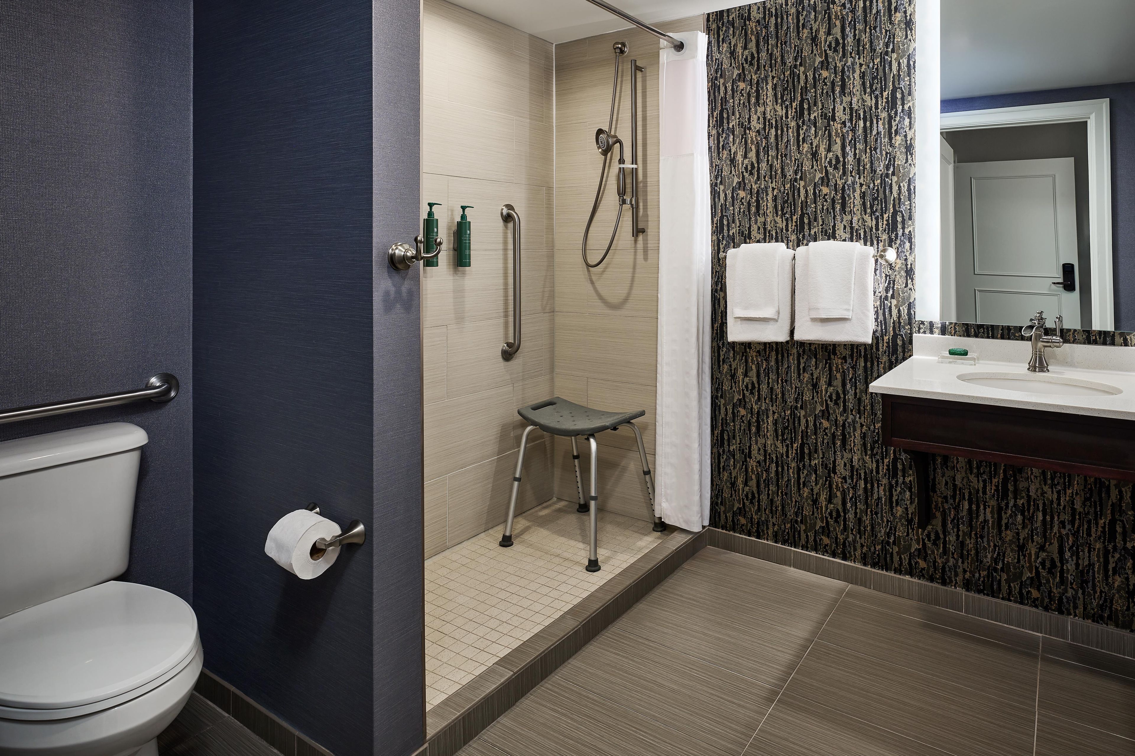 A bathroom with a toilet, a shower with a grab bar, a sink with a mirror, and two towels on the wall.