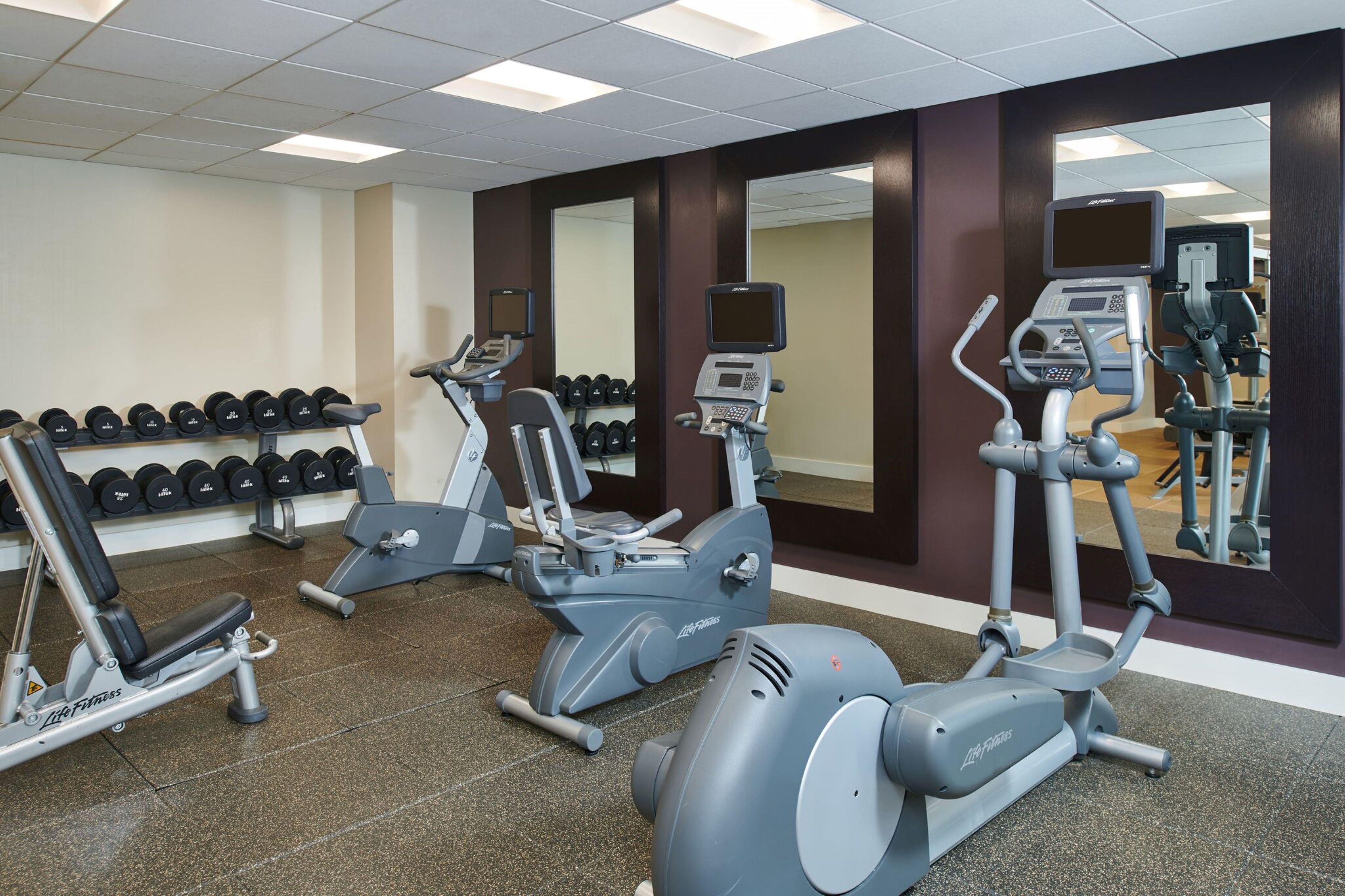 A gym with cardio machines, dumbbells, and a mirror.