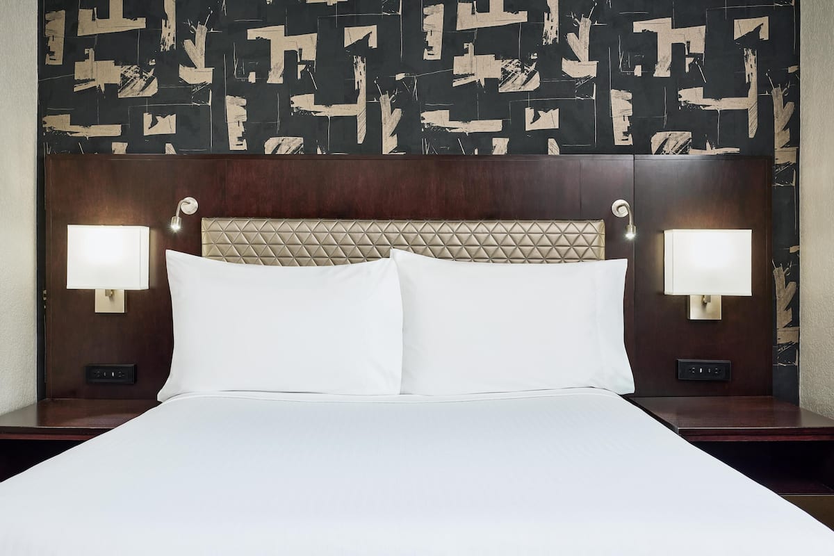 A hotel room with a bed, two bedside lamps, a headboard with a quilted design, and a wall with a geometric pattern.