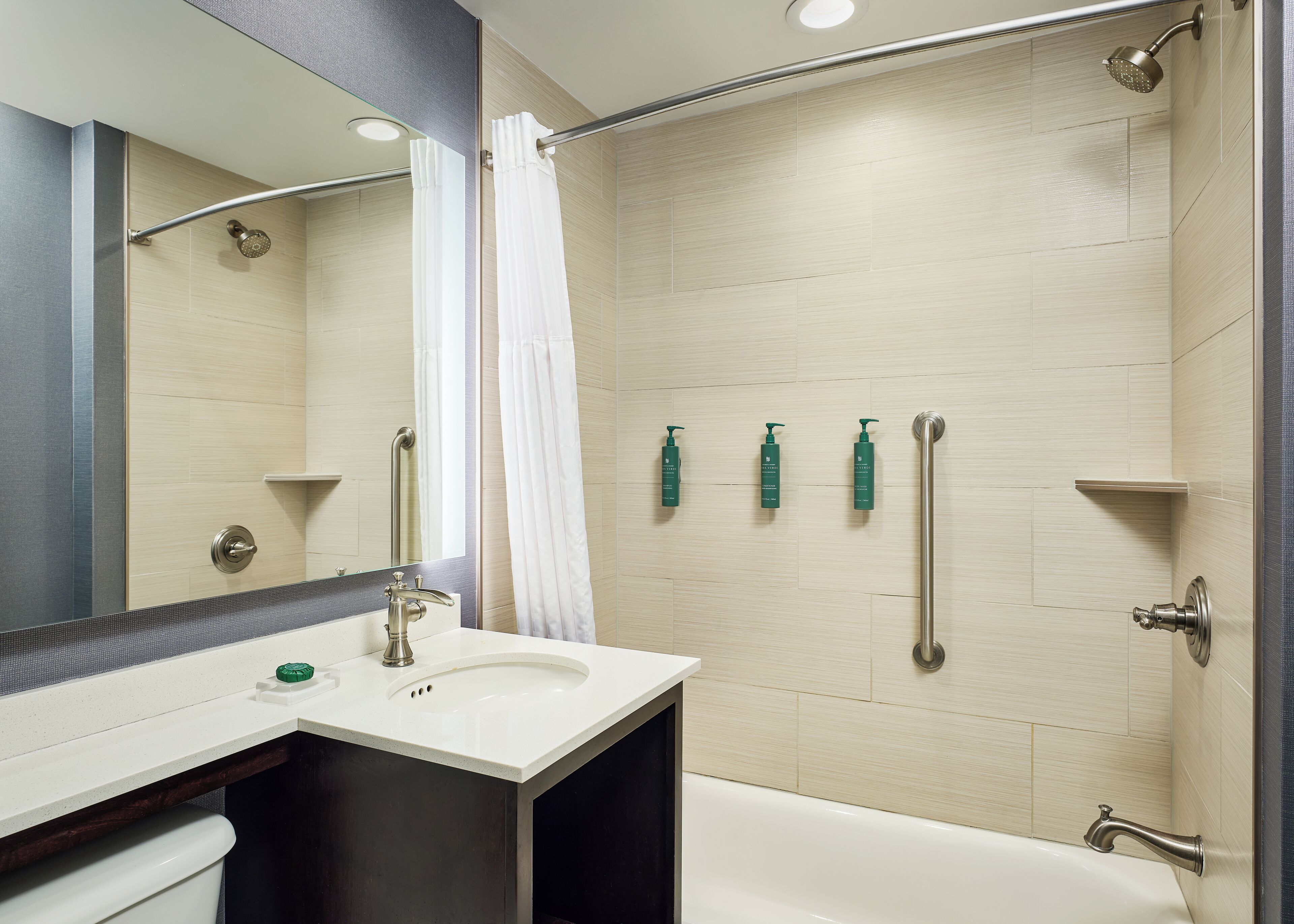 A modern bathroom with a shower, a sink, a mirror, and three toiletries on the wall.
