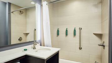 A modern bathroom with a shower, a sink, a mirror, and three toiletries on the wall.