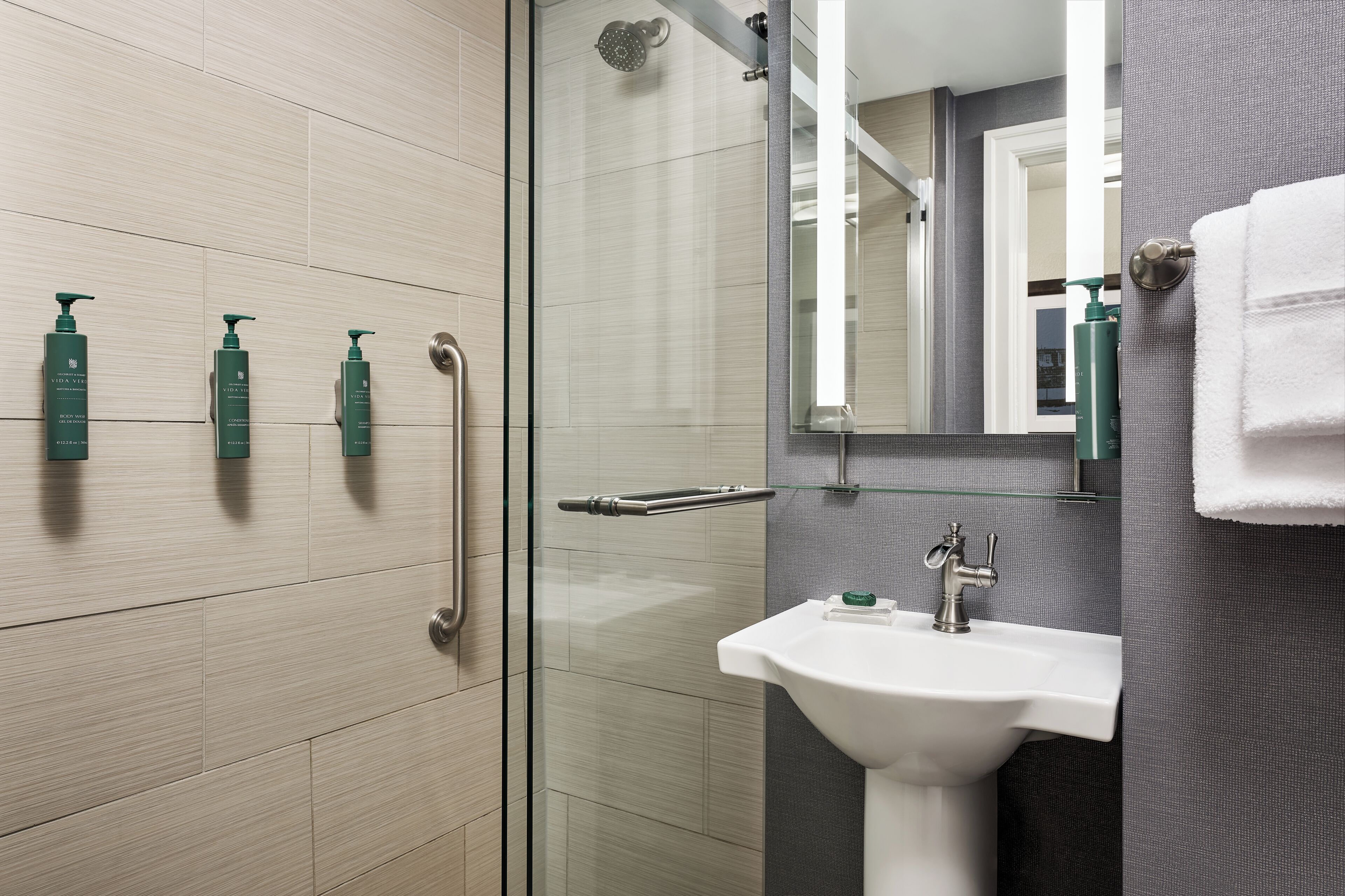 A modern bathroom with a glass shower enclosure, a white sink, and three green toiletries on the wall.
