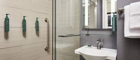 A modern bathroom with a glass shower enclosure, a white sink, and three green toiletries on the wall.