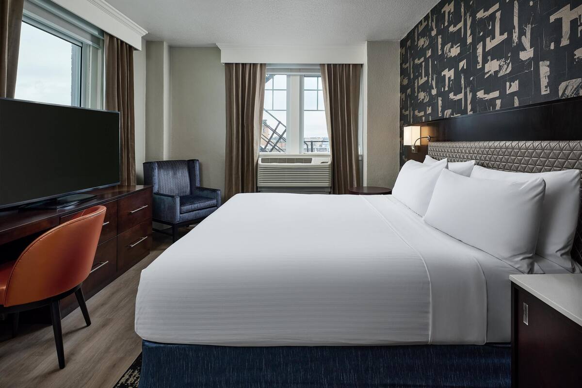 A hotel room with a large bed, a TV, a desk, and a chair.