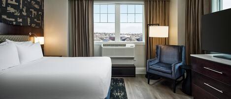 Una habitación de hotel con cama, escritorio, silla, televisión, ventana con vista y pared con diseño geométrico.