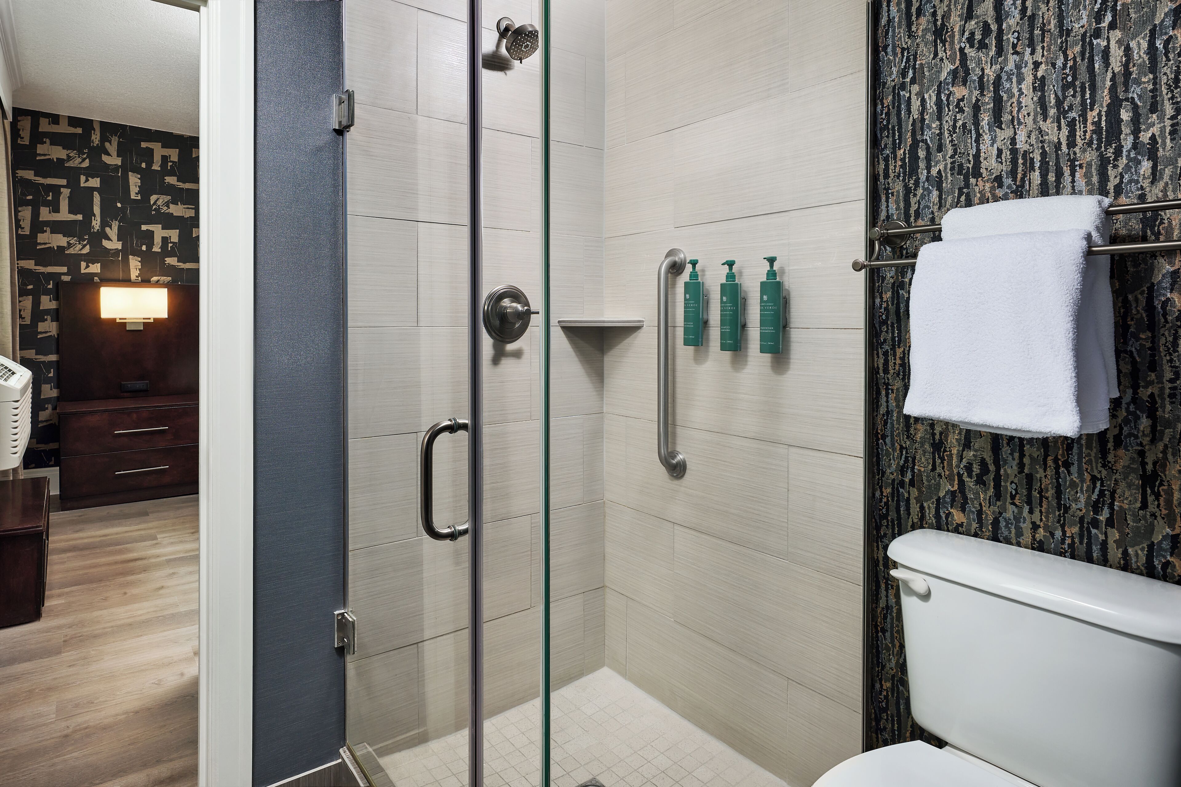 A modern bathroom with a glass shower enclosure, a toilet, and a towel rack.