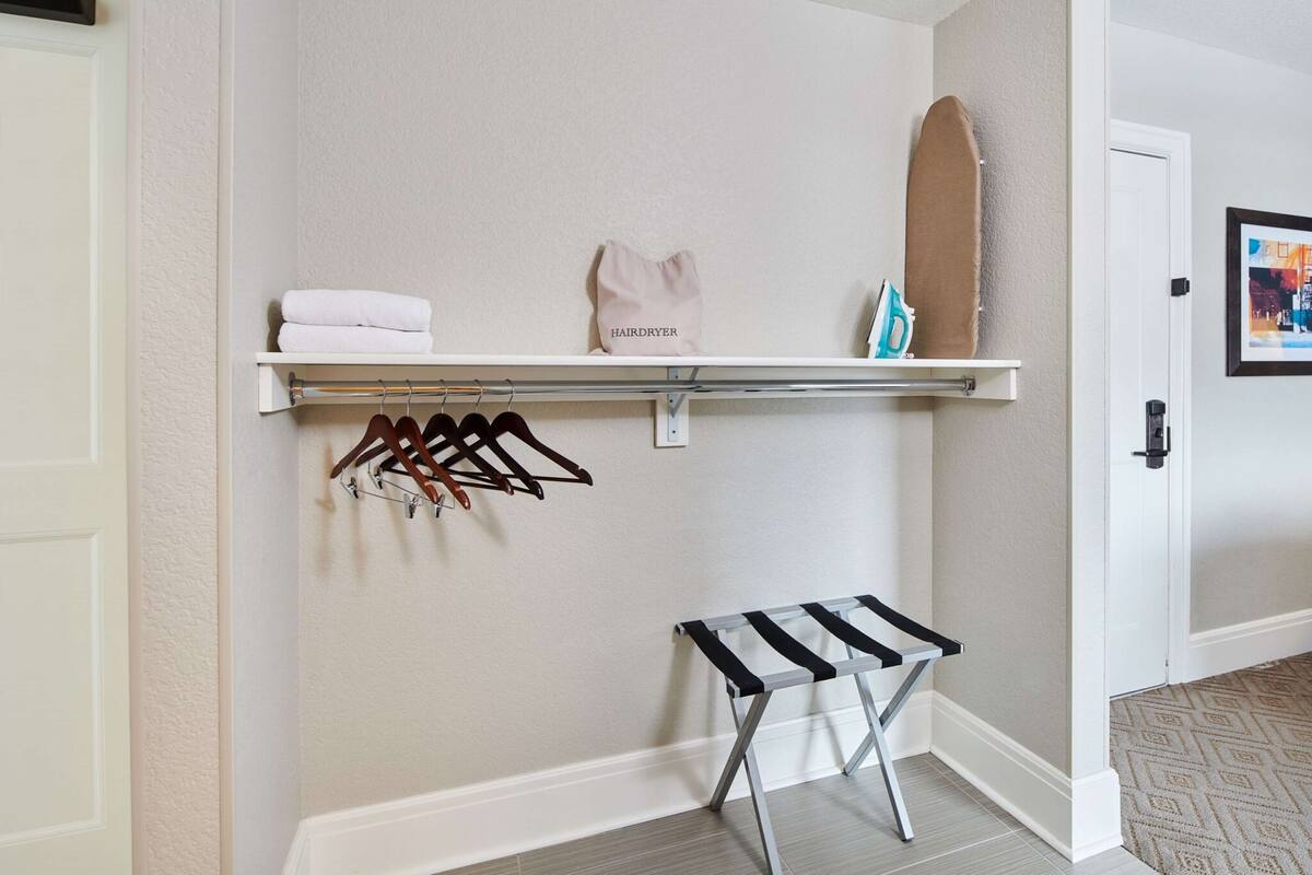 A hallway with a white door, a shelf with folded towels, a hairdryer, and a bench.