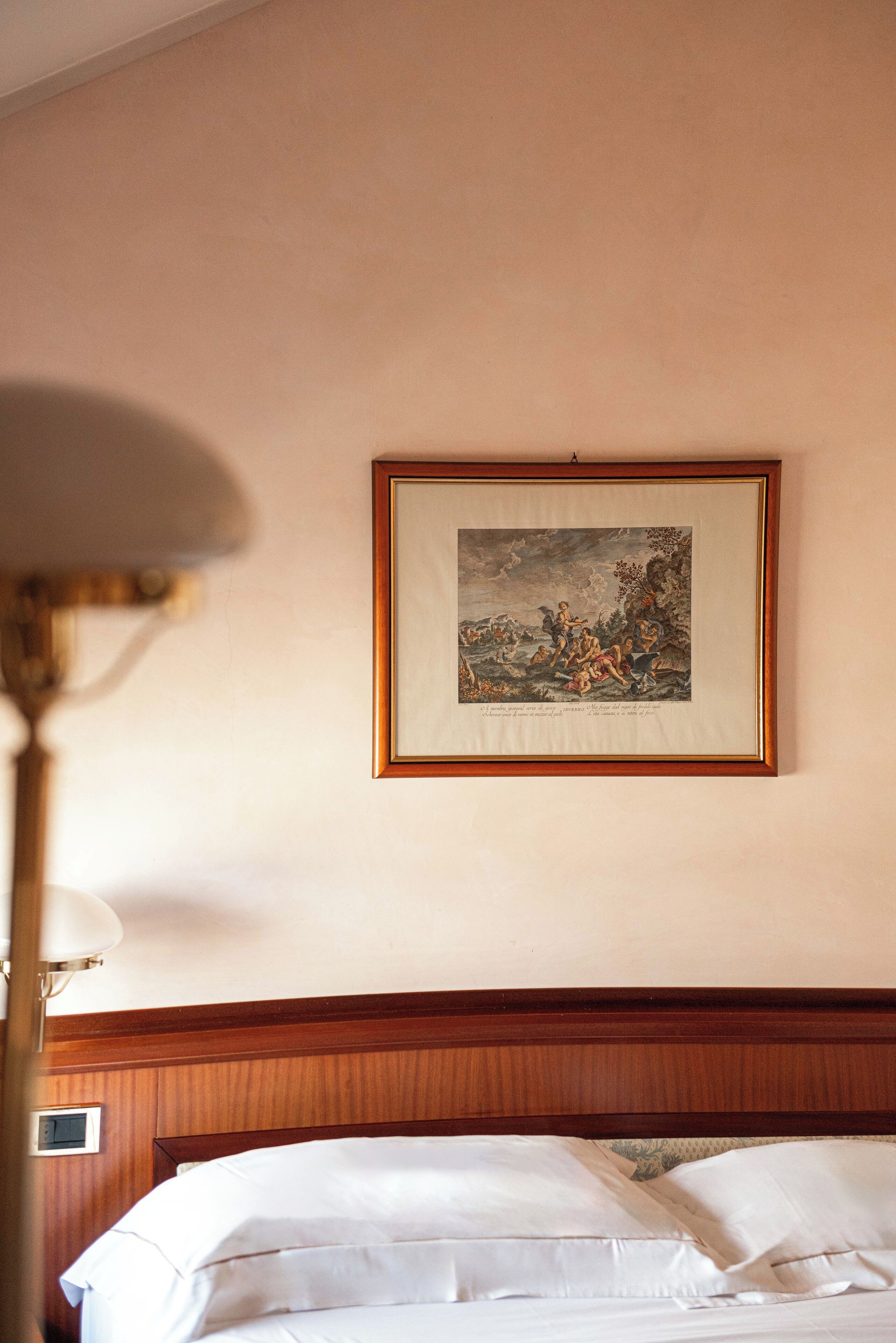 Una habitación de hotel con una cama, una obra de arte enmarcada en la pared y una lámpara.