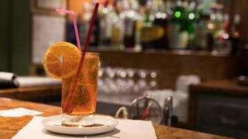 Un verre d’une boisson ambrée, décoré d’une tranche d’orange et d’une paille rose, est posé sur un sous-verre blanc, dans un cadre de bar.