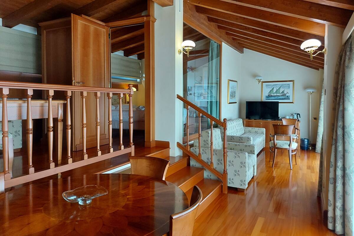 A spacious living area with a wooden staircase, a sofa, a TV, and a dining table.