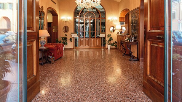 Un hall d’hôtel agrémenté d’un lustre, de portes en arc de cercle et d’un comptoir d’accueil.
