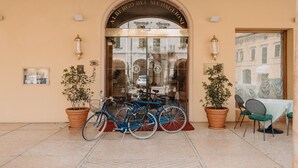 L’entrée d’un hôtel, avec une porte en verre, deux vélos garés devant et des plantes en pot de chaque côté.
