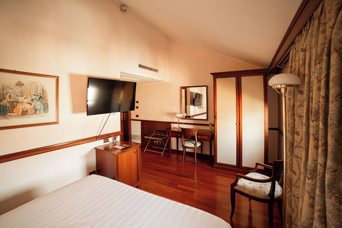 A hotel room with a bed, a desk, a chair, a television, and a wardrobe.