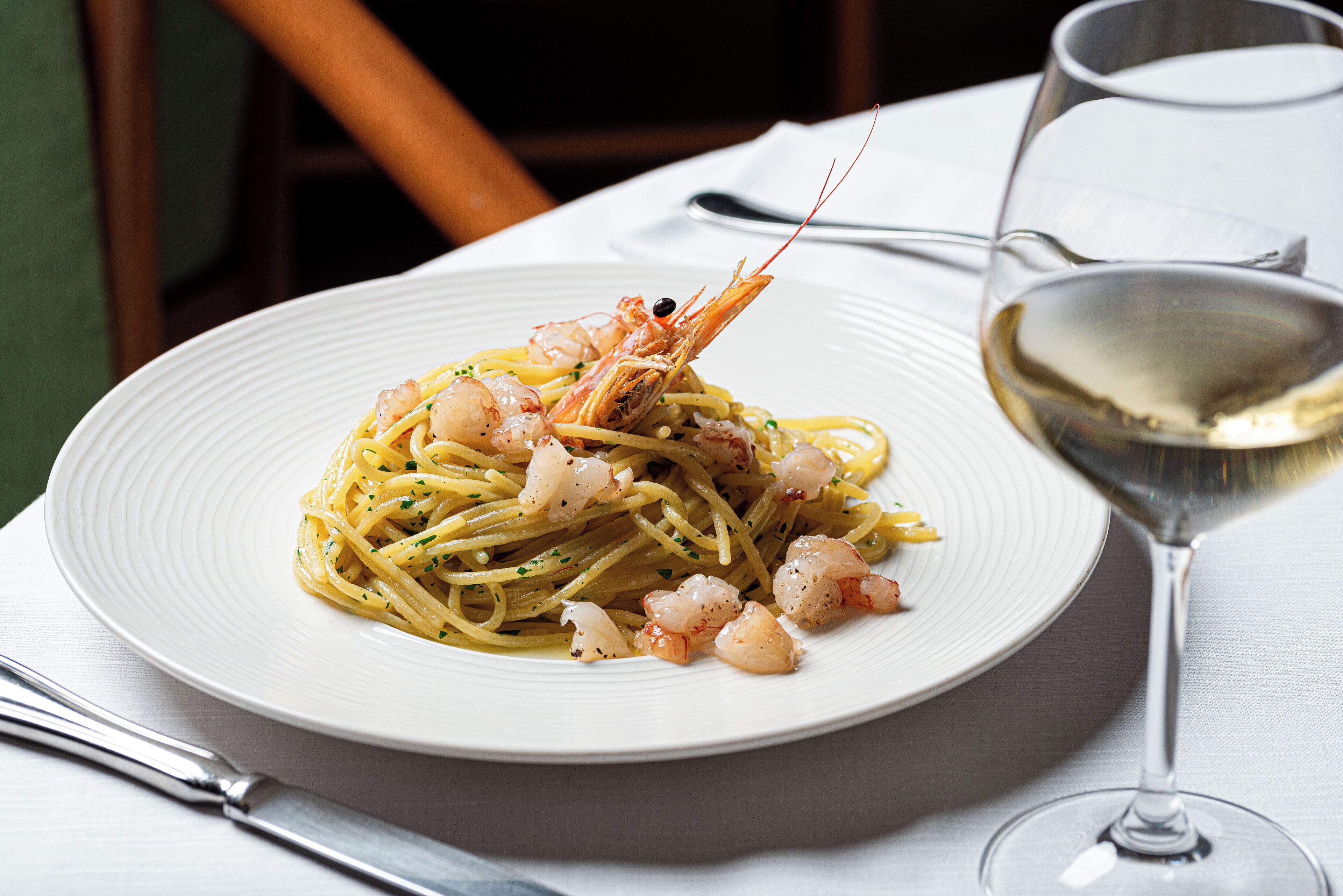 A plate of spaghetti with shrimp and a glass of white wine on a table.
