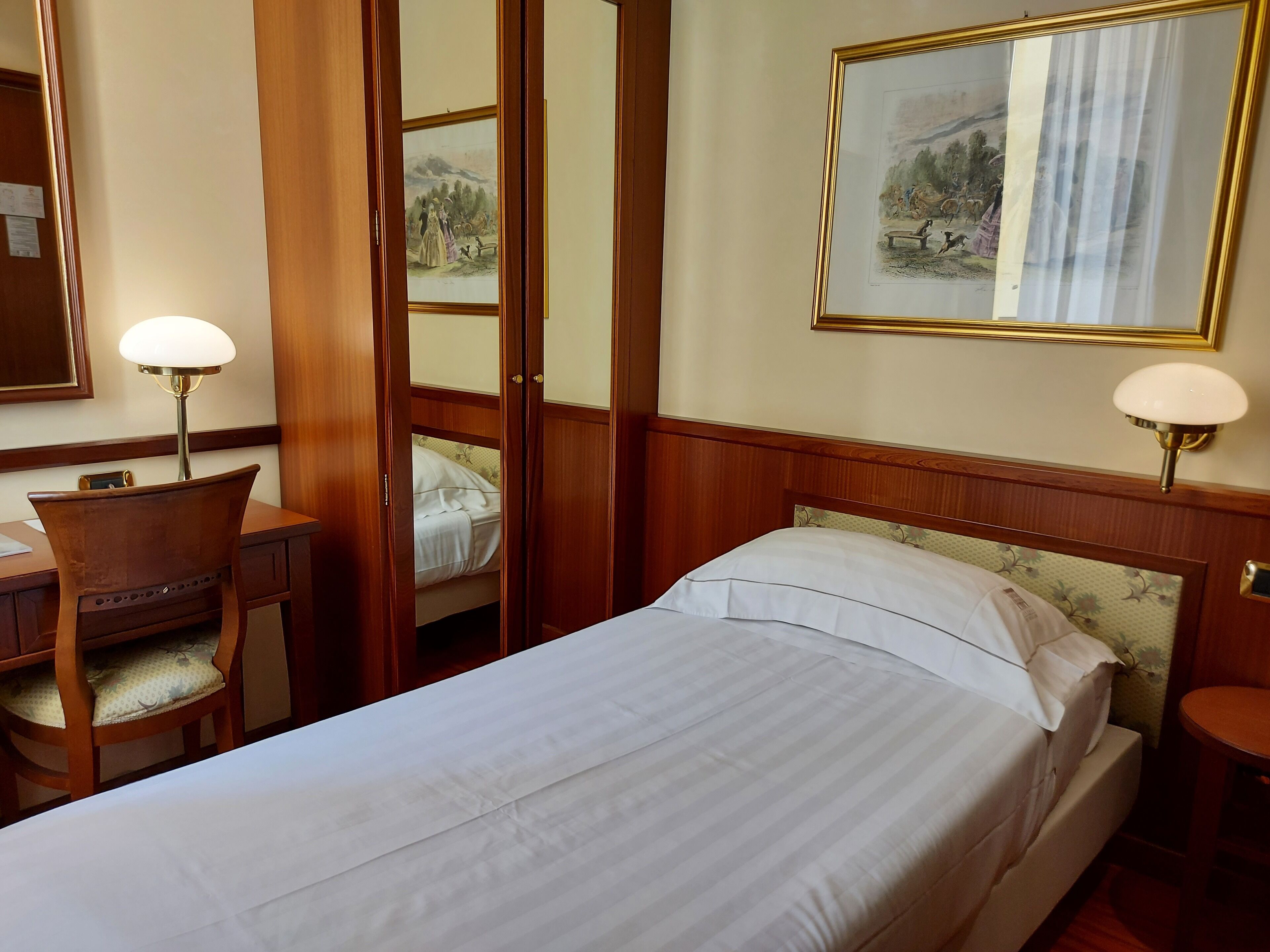 Een hotelkamer met een bed, een bureau met stoel, een lamp en een spiegel.