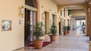 Un couloir d’hôtel agrémenté de plantes en pot, un comptoir de réception et une entrée avec une porte en verre.