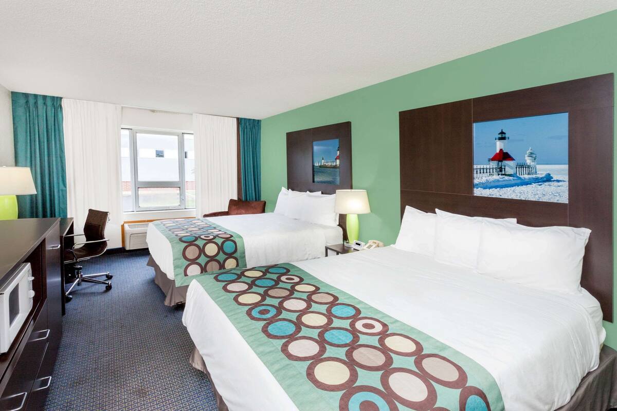 Habitación de hotel con dos camas, un escritorio, una silla y una ventana con cortinas.