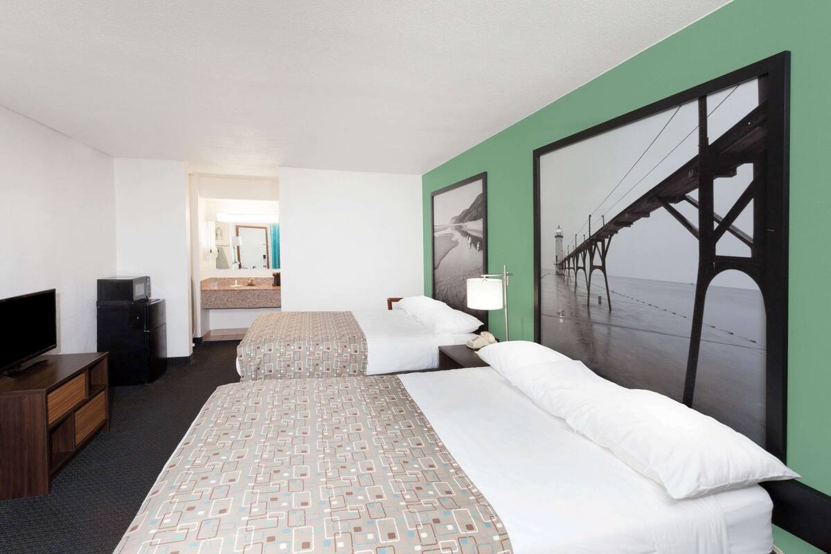 Habitación de hotel con dos camas, televisión, escritorio y baño visible a través de una puerta abierta.
