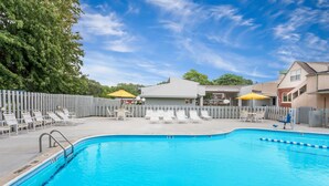 Ein Pool mit Liegestühlen und Sonnenschirmen, umgeben von einer Einfriedung und Gebäuden.