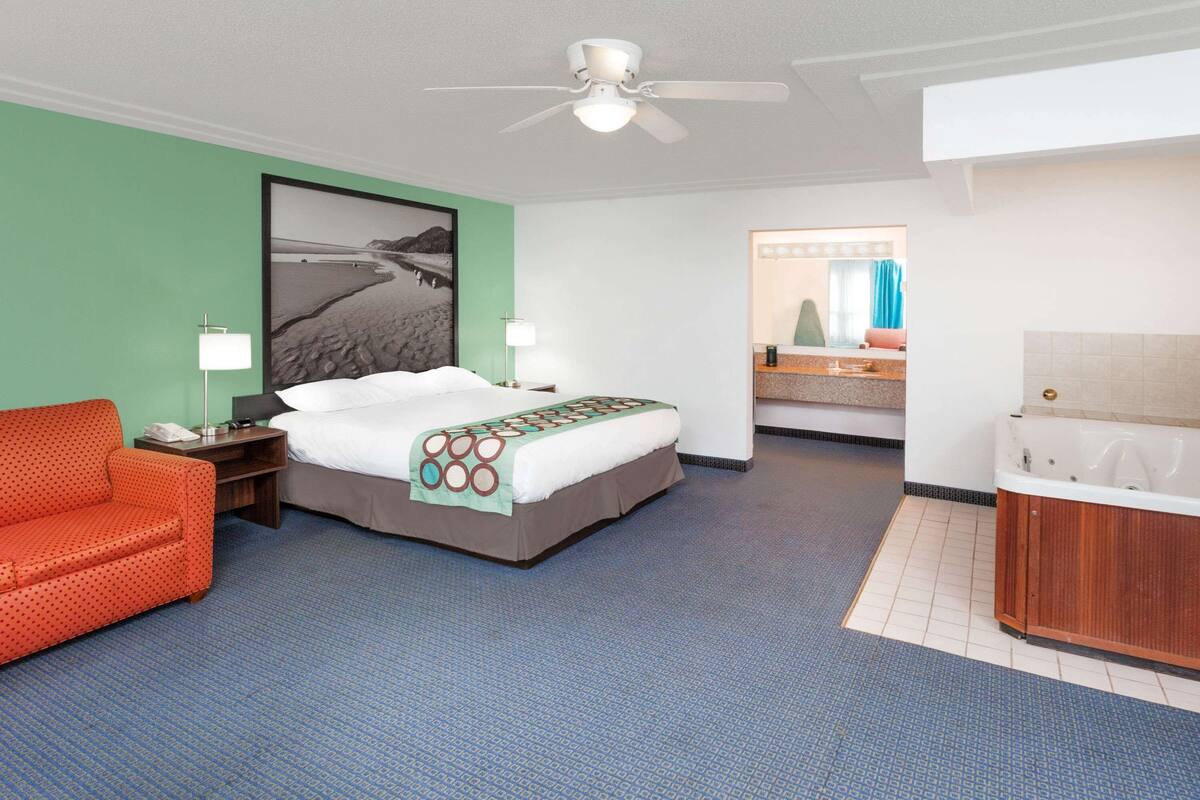 Habitación de hotel con cama, sofá rojo, baño con bañera y un cuadro grande en la pared.