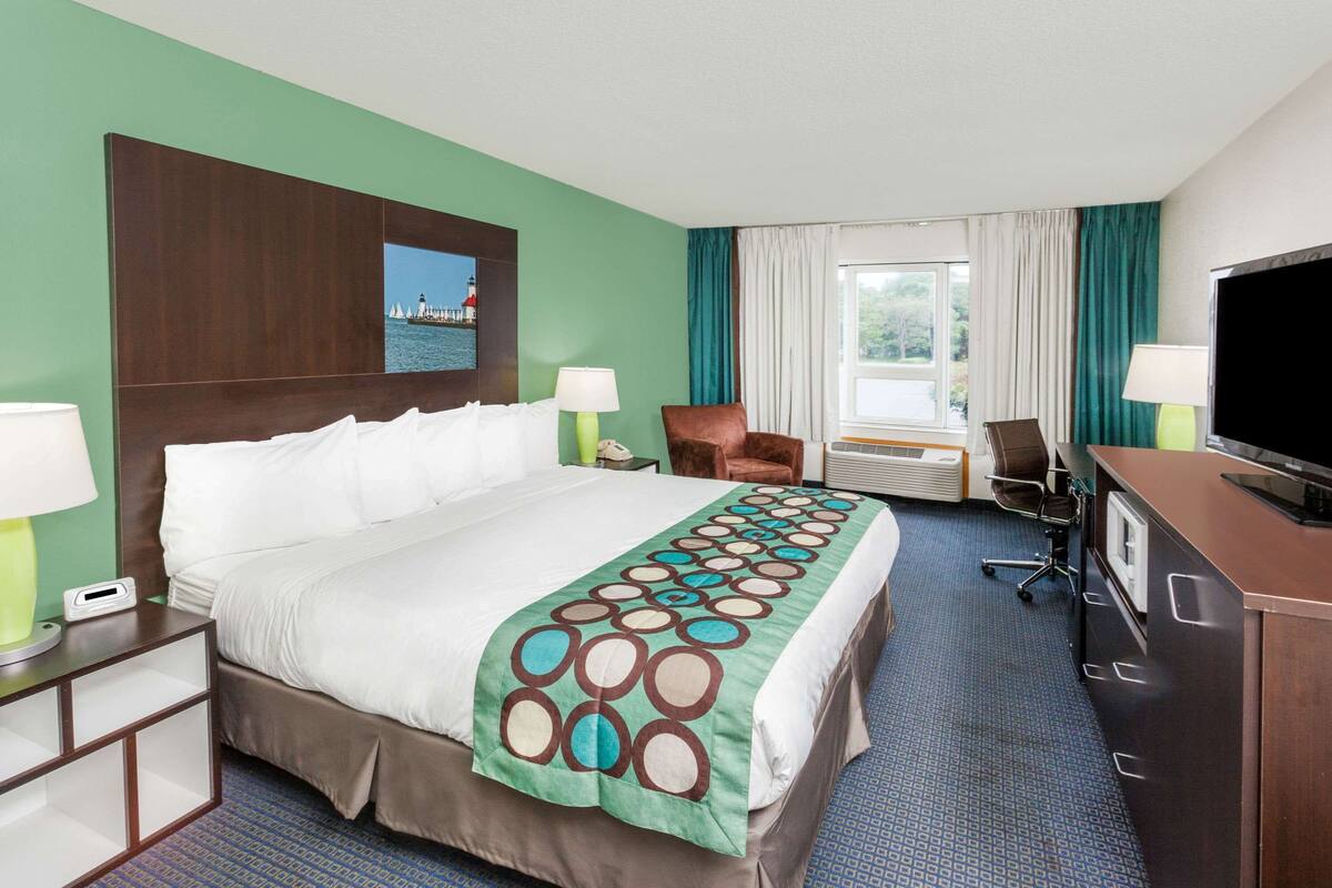Una habitación de hotel con una cama grande, un escritorio, un televisor y una ventana con cortinas.