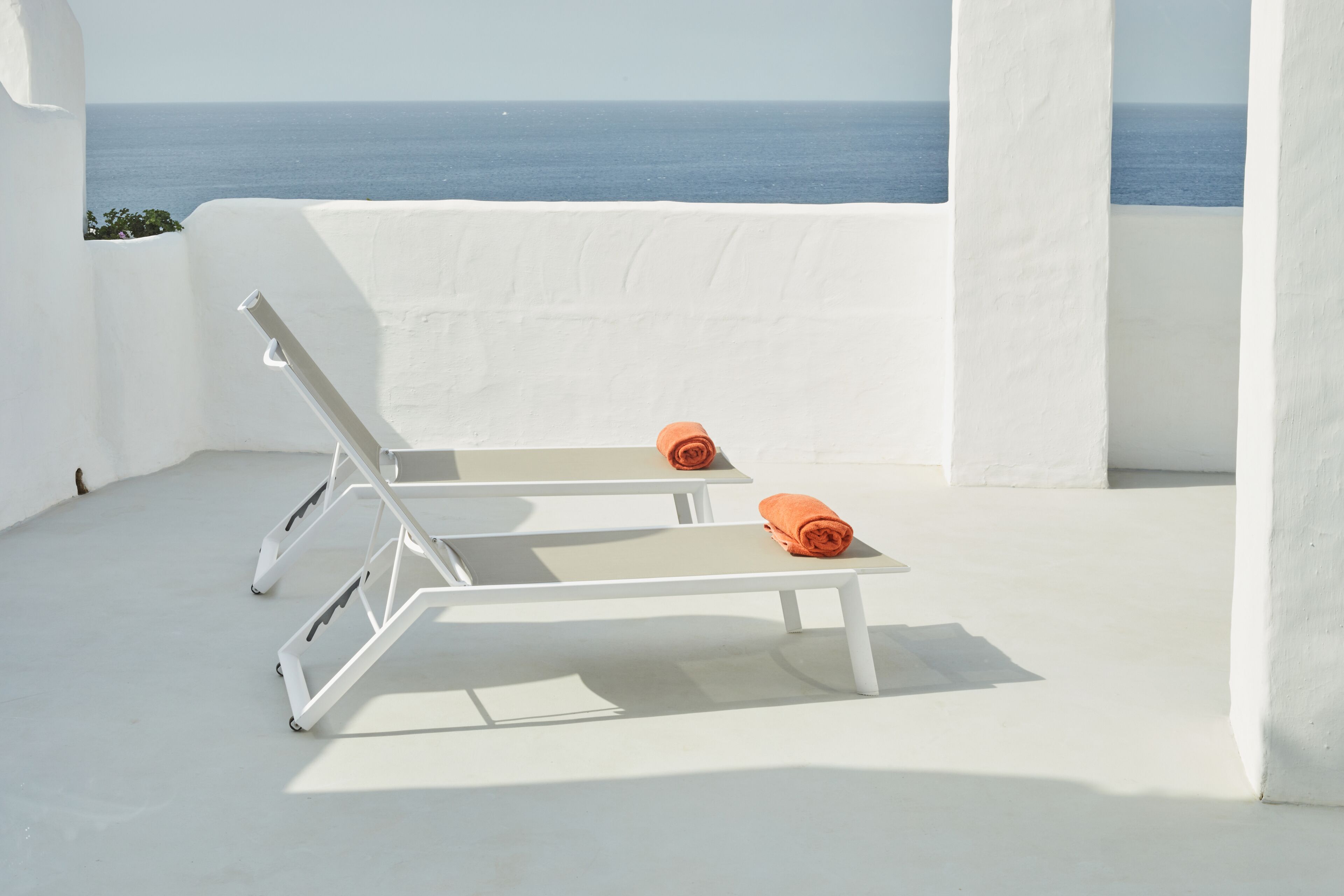 Un área de estar exterior blanca con dos sillones y toallas naranjas, con vista al mar.