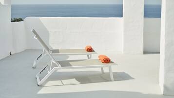 Un área de estar exterior blanca con dos sillones y toallas naranjas, con vista al mar.