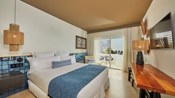 A hotel room with a large bed, a wooden desk, a balcony with a view, and a tiled wall.