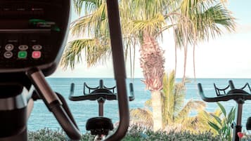 An outdoor exercise area with stationary bikes, a thatched roof, and a view of the ocean and palm trees.