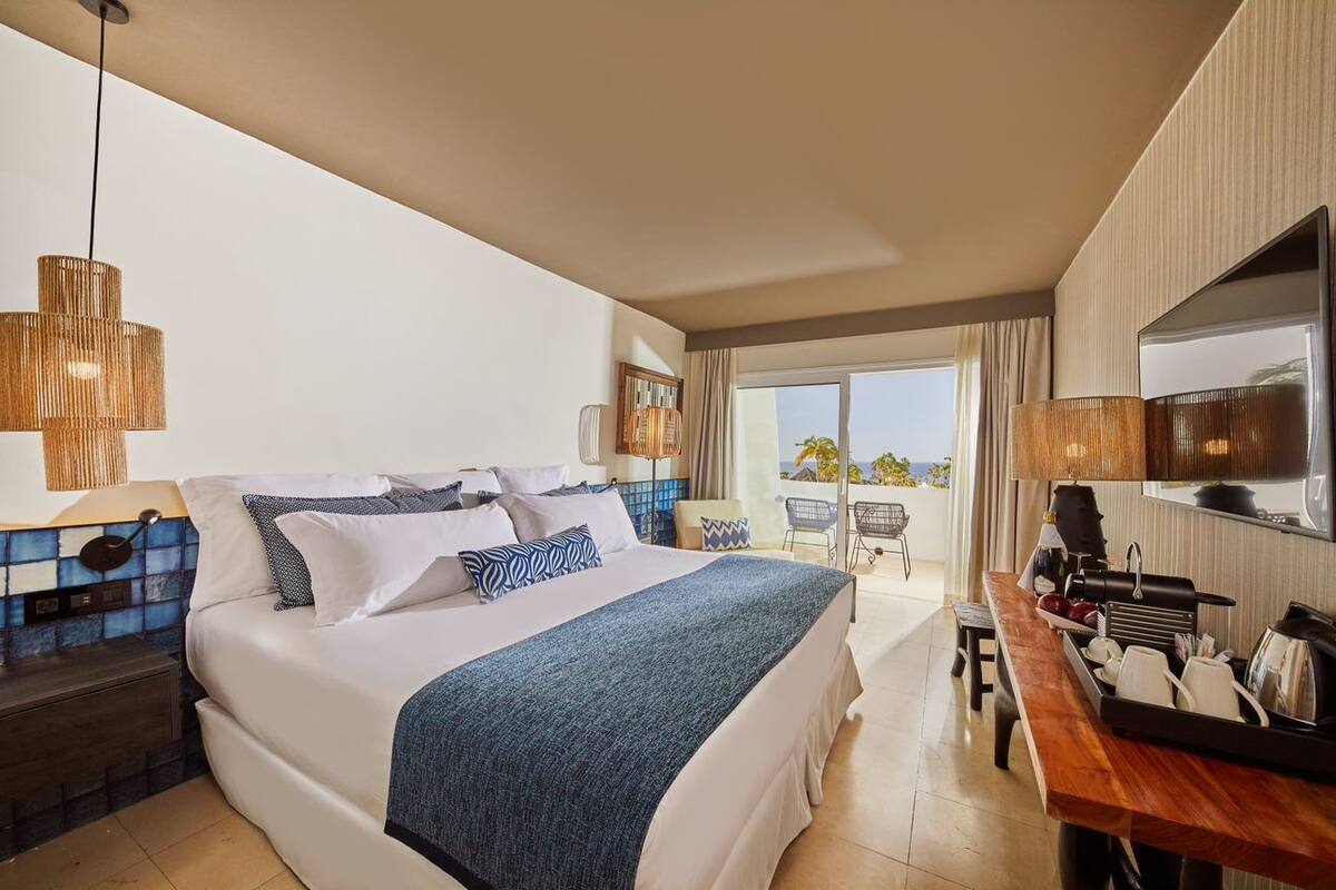A hotel room with a large bed, a desk with a coffee machine, a TV, and a balcony with a view.