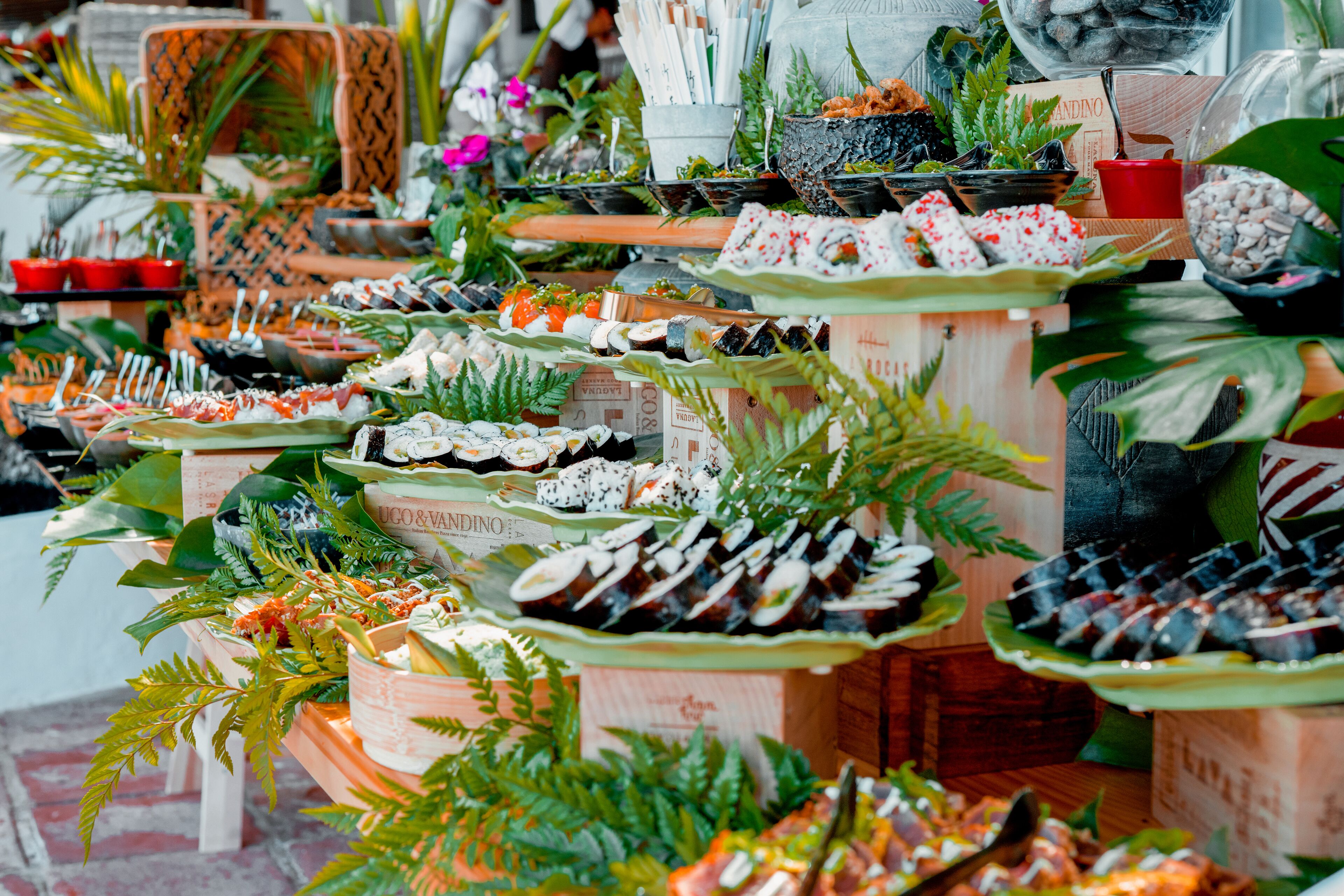 A variety of food items displayed on tables, surrounded by plants and decorative elements.