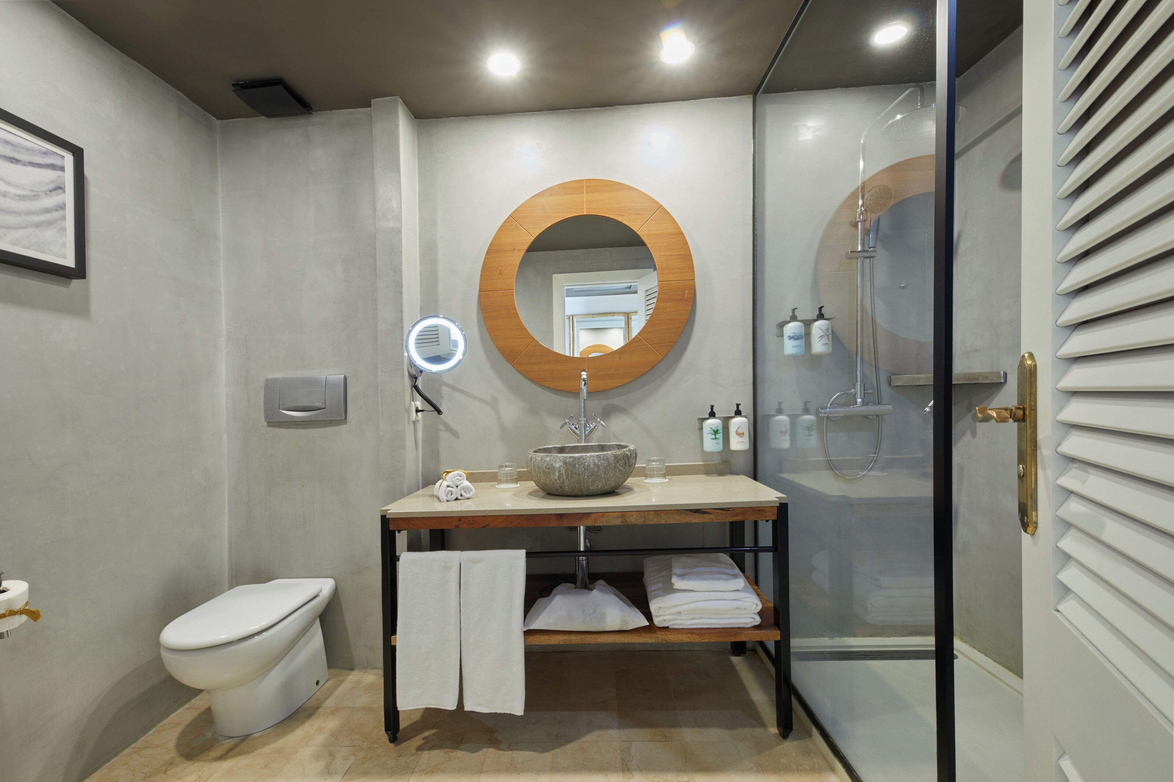 Une salle de bain moderne avec un miroir rond, un lavabo en pierre, des toilettes et une douche à parois de verre.